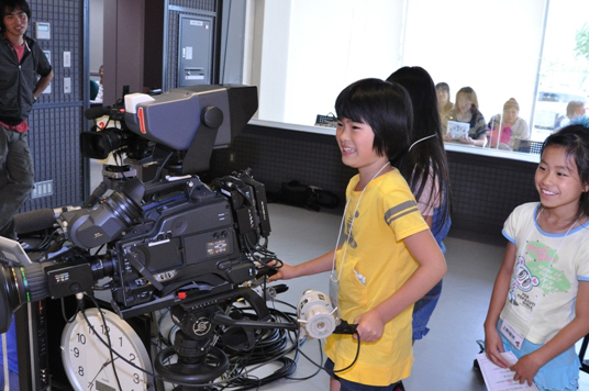 テレビカメラでキャスターの笑顔を映す子ども